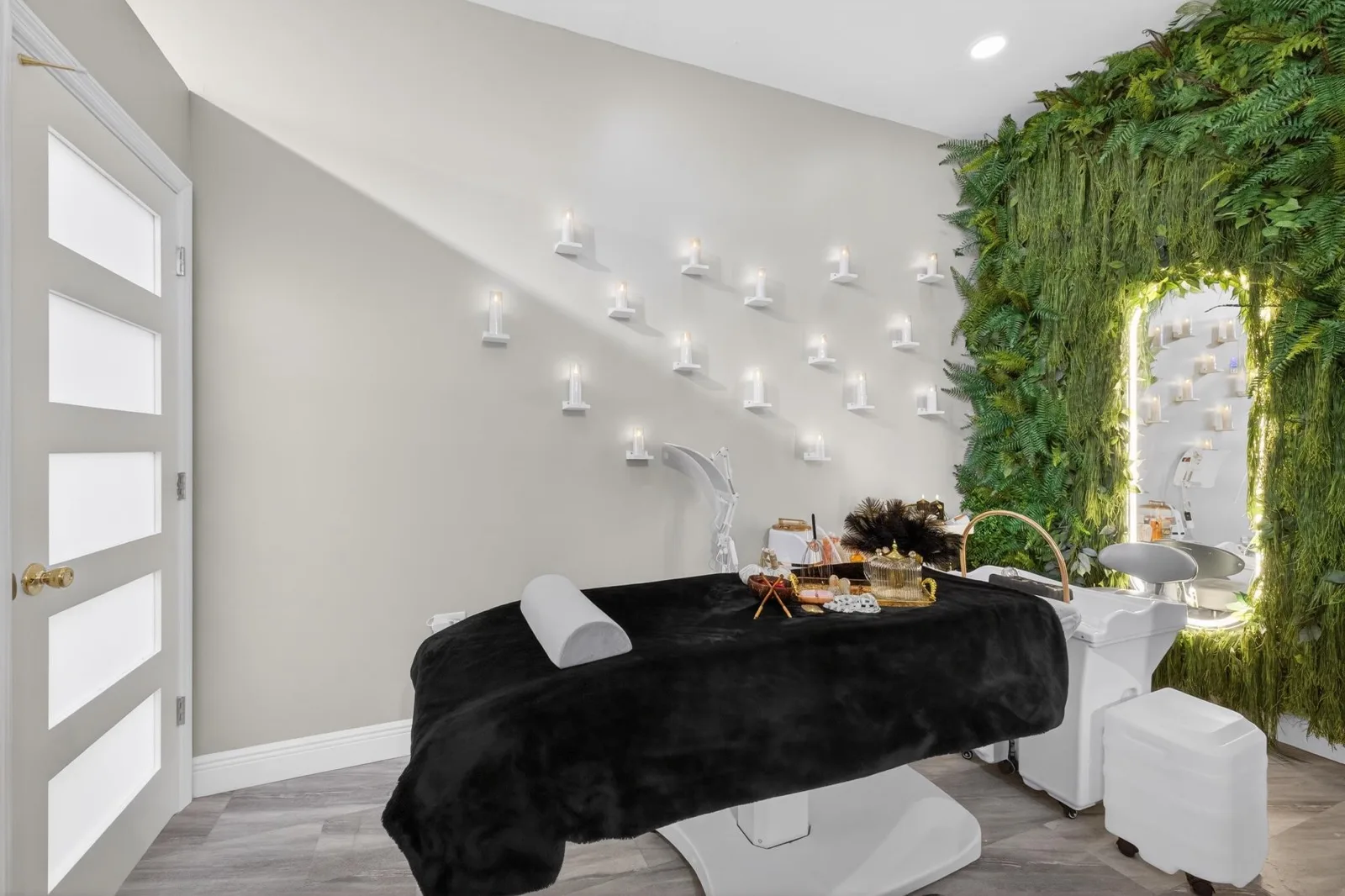 An illuminated arched mirror set into a wall of ferns above a head-spa bed