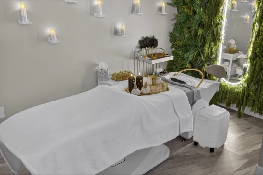 A treatment bed made up in white below rows of candle sconces, against a wall of preserved ferns