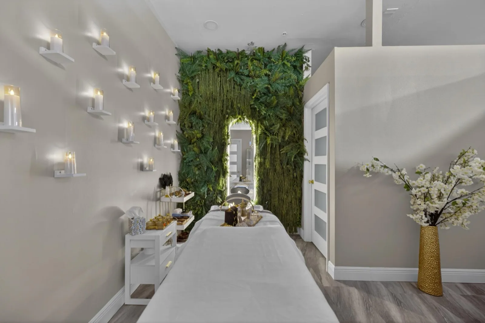 A treatment bed lit by candle sconces against a wall of preserved ferns
