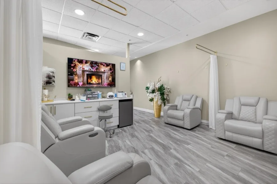 Cream IV recliners arranged around a wall screen showing a fireplace, with orchids, a treatment cabinet and a drawn white curtain