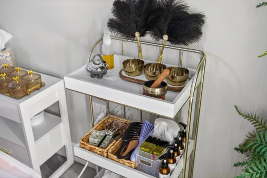 A gold-railed trolley of head-spa tools — brass singing bowls, black feather fans, oils and gua sha stones