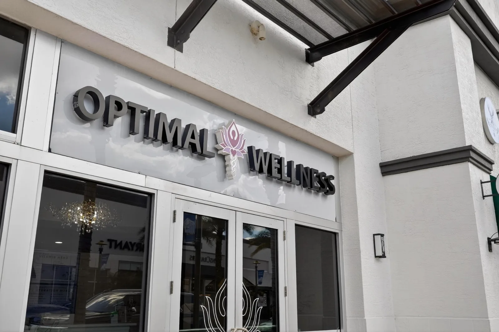 The Optimal Wellness sign mounted on the white board-and-batten shopfront at The Shops at Wiregrass