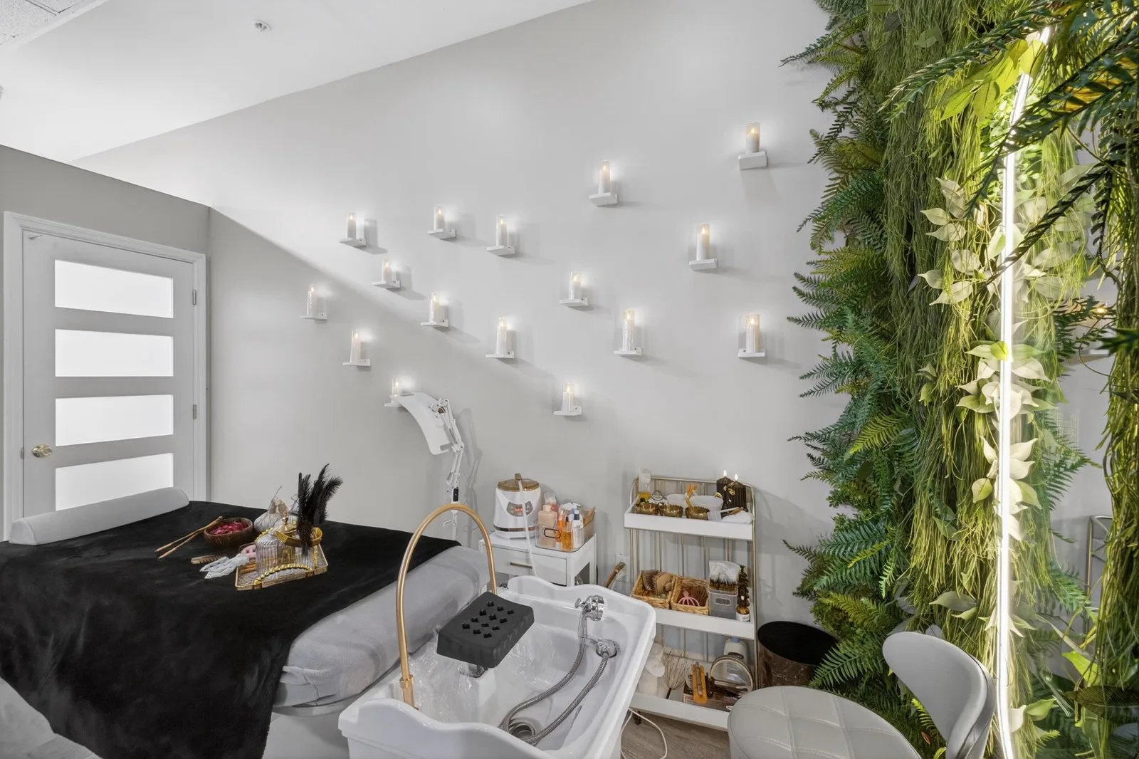 A head-spa bed dressed in black towels beside a fern wall and a trolley of tools