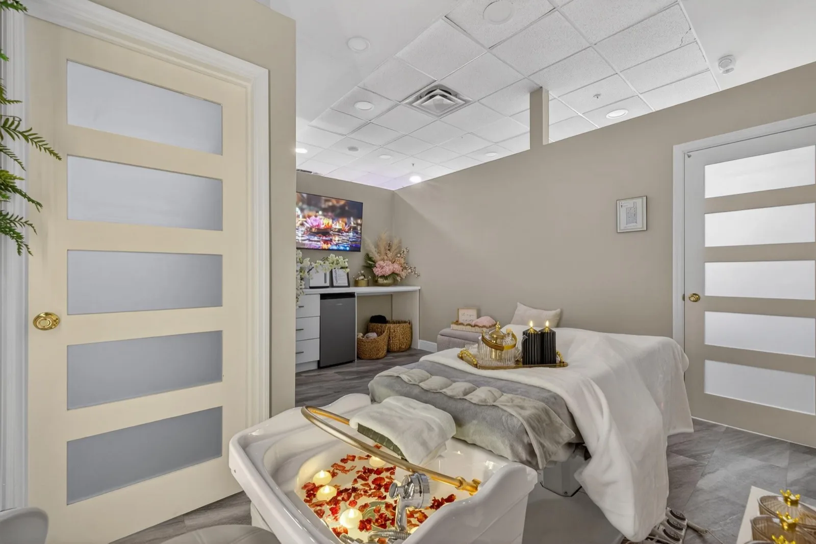 A made-up treatment bed beside gold-framed doors, with a tray of petals and candles